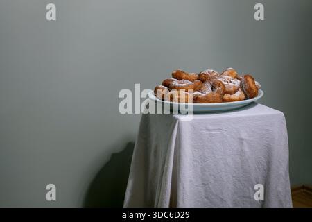 Fresh homemade donuts dusted with powdered sugar served on blue plate. Minimalist composition with white tablecloth against neutral background. Stock Photo