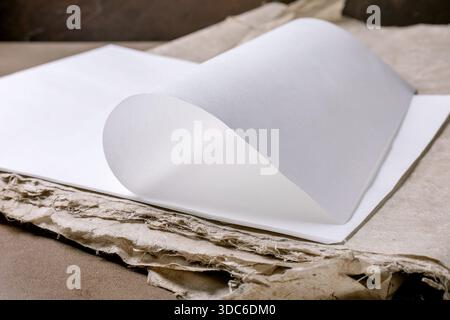 Closeup blank white rice and mulberry paper sheet with curled page on recycled cardboard background. Minimalist composition with clean paper and textu Stock Photo