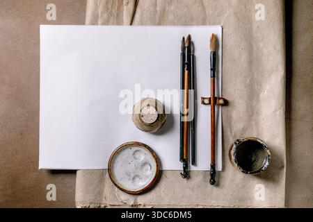 Traditional Chinese calligraphy tools on white paper. Brushes ink stone and ink container arranged on craft rice and mulberry paper background. Artist Stock Photo