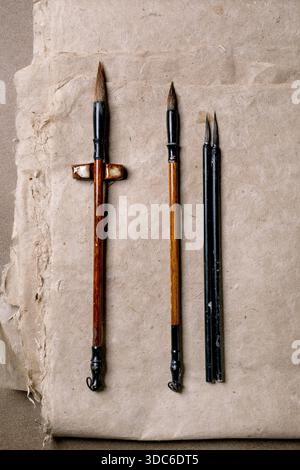 Traditional Chinese calligraphy brushes with wooden handles on aged handmade mulberry paper. Flat lay of three different sized brushes tools for orien Stock Photo