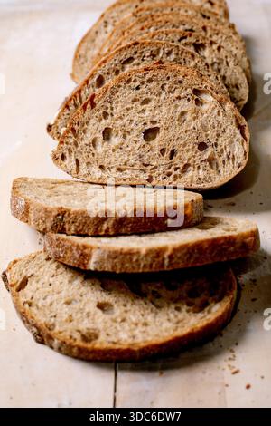Slices of rustic whole grain bread with porous texture and crunchy crust on wooden background. Closeup of artisanal sourdough bread perfect for breakf Stock Photo