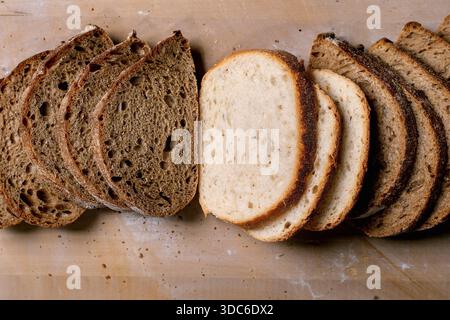 Sliced white and rye bread loaves on rustic brown wooden background. Fresh homemade bakery products showing different bread varieties texture and colo Stock Photo