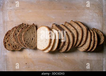 Assortment of freshly sliced bread including white whole grain and rye arranged in row on wooden cutting board. Dark and light bread varieties for san Stock Photo