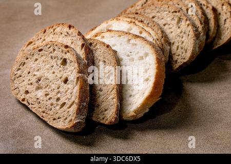 Sliced artisan bread loaf with mixed white and brown pieces arranged on brown background. Fresh homemade bread displaying soft texture and crust. Stock Photo