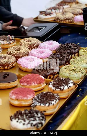 Variety of glazed donuts with different toppings arranged on gold tray. Collection includes chocolate pink pistachio flavors with sprinkles nuts choco Stock Photo