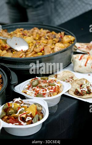 Mexican street food feast with chicken skillet corn tacos jalapenos. Containers filled with nachos meat vegetables topped with sour cream red sauce. T Stock Photo