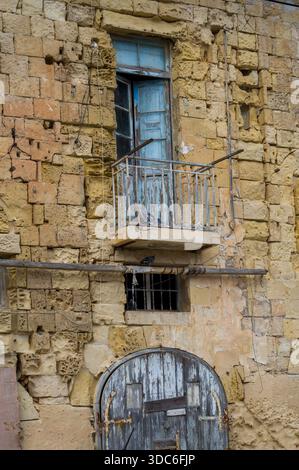 A weathered stone building shows its age with crumbling walls, a barred window, and a balcony door ajar. Pigeons perch, adding life to the decaying fa Stock Photo
