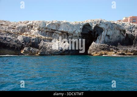 Coastal limestone cliff with a large sea cave on the Sicilian shoreline, shaped by marine erosion above deep blue Mediterranean waters Stock Photo