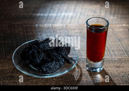 Homemade dark damson plum brandy in glasses on a wooden table, close up. Drink from dry plums Stock Photo