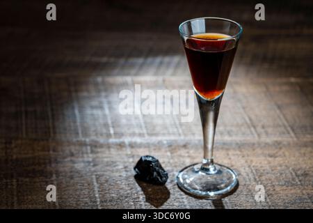 Homemade dark damson plum brandy in glasses on a wooden table, close up. Drink from dry plums Stock Photo