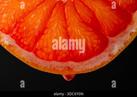Slice of red grapefruit with juice drops on a black background, macro photography. Texture fresh citrus fruit, close up Stock Photo