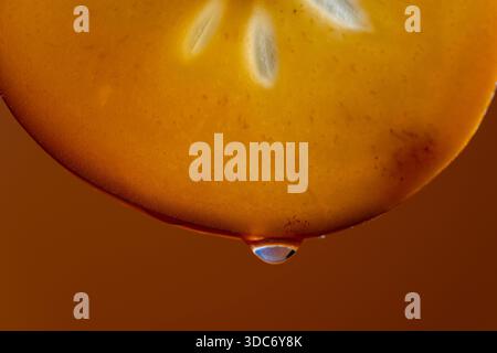 Slice of persimmon with juice drops on a orange background, macro photography. Texture fresh fruit, close up Stock Photo