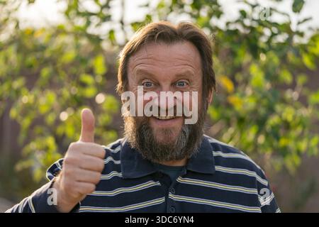 Portrait of a smiling senior man. Elderly bearded caucasian male in nature. Face bearded male dreams of solving issues, close up. Positive man giving Stock Photo