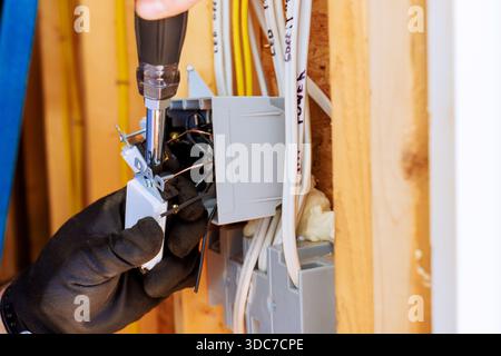 An electrician using screwdriver to connect wires inside an electrical panel in residential setting. Stock Photo