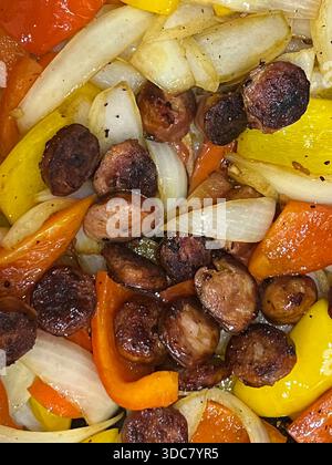 Chopped onions and colorful peppers cook in a frying pan with sliced sausage. The dish is prepared for a meal at home in a kitchen setting. Stock Photo