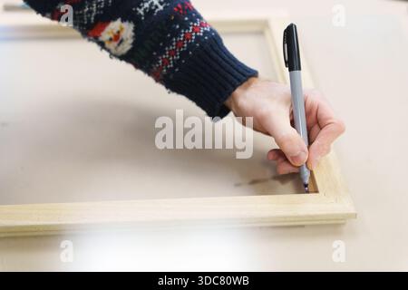 Hand of a technician using a marker to label a wooden picture frame in a workshop. High quality photo Stock Photo