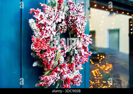 Winter charm and festive texture appear in a decorative Christmas wreath with frosted red berries, pine branches and cones hanging on a doorway, glowi Stock Photo