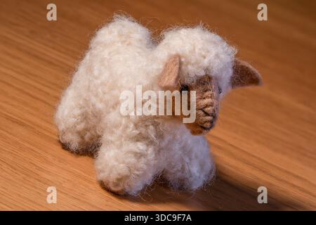 A fluffy white, sheep-shaped plush toy with a detailed brown face and ears is sitting on a polished wooden surface. Stock Photo