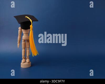 The image features a wooden artist's mannequin wearing a miniature graduation cap and yellow tassel on a blue background. Stock Photo