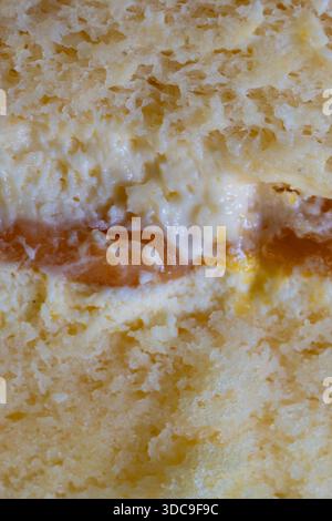 A macro shot reveals the distinct layers of a soft, yellowish sponge cake, creamy white frosting, and a vibrant orange fruit jam. Stock Photo