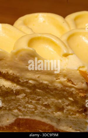 A close-up vertical shot of a dessert cake, revealing layers of light sponge and thick yellow cream frosting with decorative swirls. Stock Photo