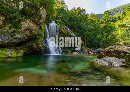 Majestic cascading waterfall surrounded by lush greenery evokes tranquility and wonder in Slovenias pristine Soca Valley Stock Photo