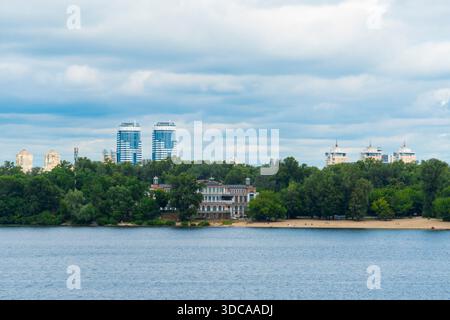 Scenic view of a wide river with a sandy beach, lush green trees and modern skyscrapers in the background under a dramatic cloudy sky Stock Photo