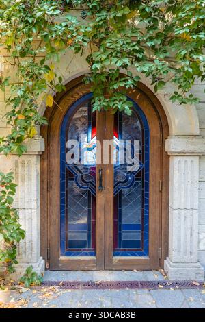 Vintage arched wooden entrance door with decorative blue stained glass window and green climbing ivy. Elegant classical architecture and garden design Stock Photo