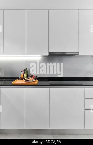 Contemporary kitchen with glossy white cabinets, black marble countertop, and under-cabinet LED lighting Stock Photo