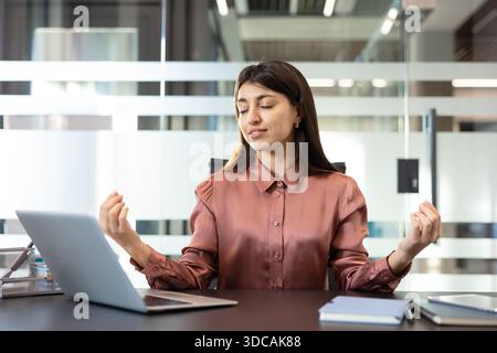 Young businesswoman practicing mindful breathing at her modern office desk, finding calm and reducing work stress to boost focus, balance, and mental well-being Stock Photo