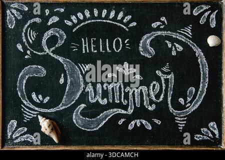 Summer theme. Chalk handwritten decorative lettering Hello summer on blackboard, decorated by seashells shells Stock Photo