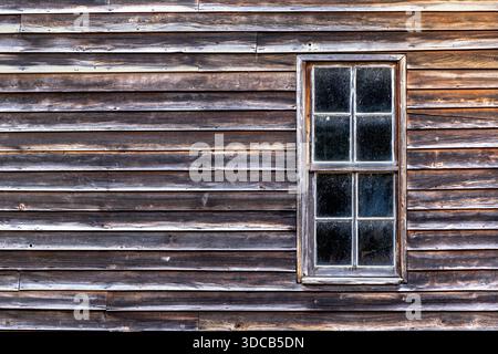 Old barn wooden exterior wall and window shows the years of weathered effect on the wooden slats and the windswept glass window. Good for placement of Stock Photo