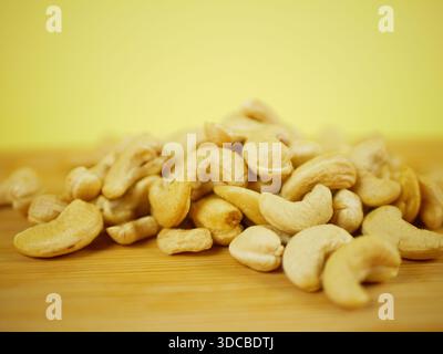 Raw cashew nuts piled on a wooden board against a bright yellow background for clean ingredient presentation and healthy snack visuals, Pro Photo Stock Photo
