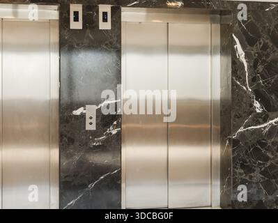 Two elevator doors stand in a building with dark marble walls. The setting shows a clean and modern environment for accessing different floors of the Stock Photo