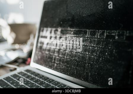 Old laptop showing heavy dust and grime accumulation on its black screen and keyboard, concept of abandonment, neglect, outdated technology, and a forgotten device Stock Photo