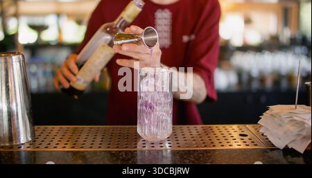 Mixologist work. Making cocktail. Bartender pouring sweet aroma color syrup from metal jigger to glass. Flavored refreshing drink. Stock Photo