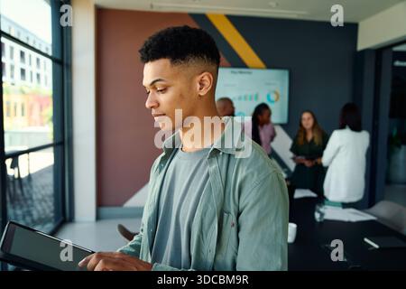 Focused young businessman using tablet with colleagues in background in boardroom at office Stock Photo