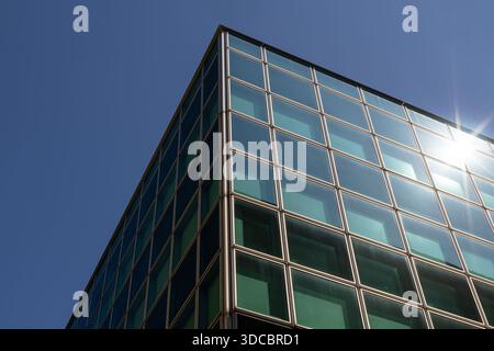A sharp, angled shot of a glass-clad office building showing a grid of windows, steel frames, and bright sunlight reflecting on the facade. Clean, con Stock Photo