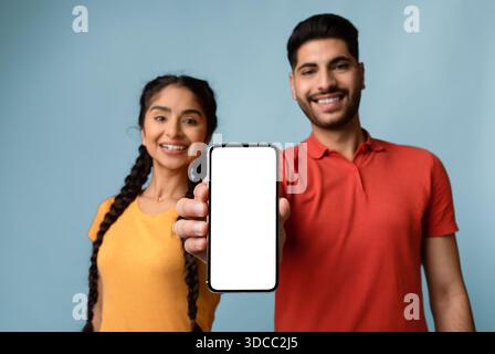 Smiling Young Couple Showing a Smartphone With a Blank Screen in Front of a Blue Background Stock Photo