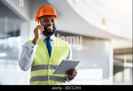 Construction Worker Talking on Phone While Using Tablet in Office Setting Stock Photo