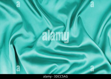 Crumpled, wrinkled turquoise colored glossy silk satin texture. Shiny smooth fabric with soft folds, cloth with wave drapery. Elegant and rich backgro Stock Photo