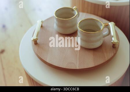 Two stylish white mugs resting on a wooden tray with metallic handles. Concept of modern interior design, comfortable home lifestyle, and simple elega Stock Photo