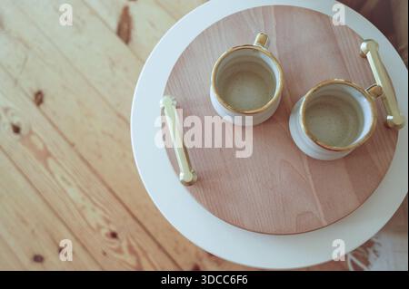 Ceramic mugs on a wooden serving tray with gold details in a festive room. Concept of holiday warmth, Christmas breakfast for two, and elegant winter Stock Photo