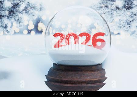 New Year 2026 concept. Red numerical digits 2026 inside a festive snow globe sitting in a snowy, winter landscape with bokeh lights. Symbolizes future Stock Photo