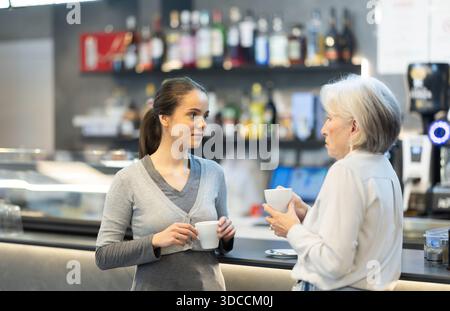 Girl and senior woman is having nice conversation, spending time in cafe Stock Photo