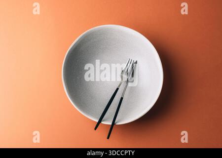 Empty grey plate with fork and knife on warm brown background. Top view, flat lay. Stock Photo