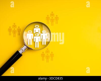 Magnifying glass focusing on humanoid AI team icons among people figures group, symbolizing artificial intelligence in recruitment, automation in job Stock Photo