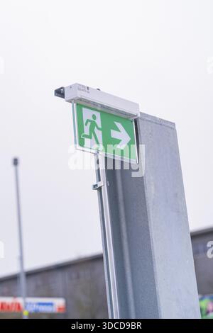 Green emergency exit sign with directional arrow on a metal post, parking garage construction with charging infrastructure, Calw, Germany Stock Photo