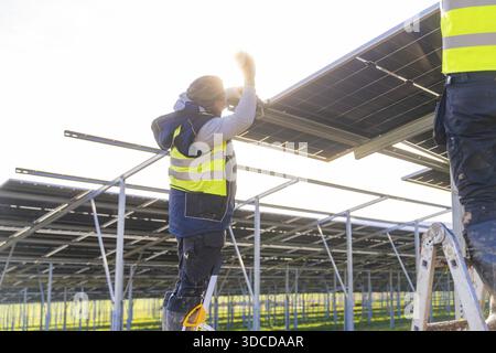 Worker installing solar panels in sunlight on metal frame, Energiewende, construction of PV open space, Baden-Wuerttemberg, Germany Stock Photo