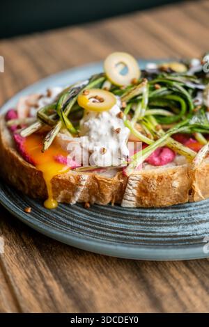 Appetizing lunch. Portion dish. Sandwich with vibrant toppings serving on plate. Food with green grilled leaves beetroot olives yolk sauce. Stock Photo